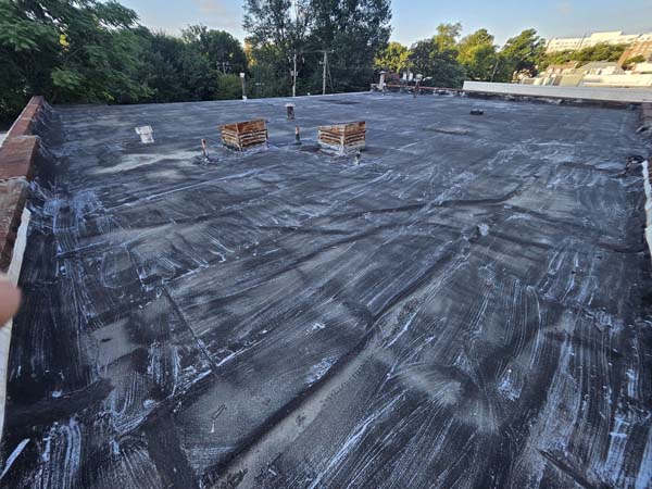 Aged modified bitumen roof at 2330 Columbia Pike in Arlington, Virginia, showing weathered surface, previous coating residue, and timber curbs before silicone restoration