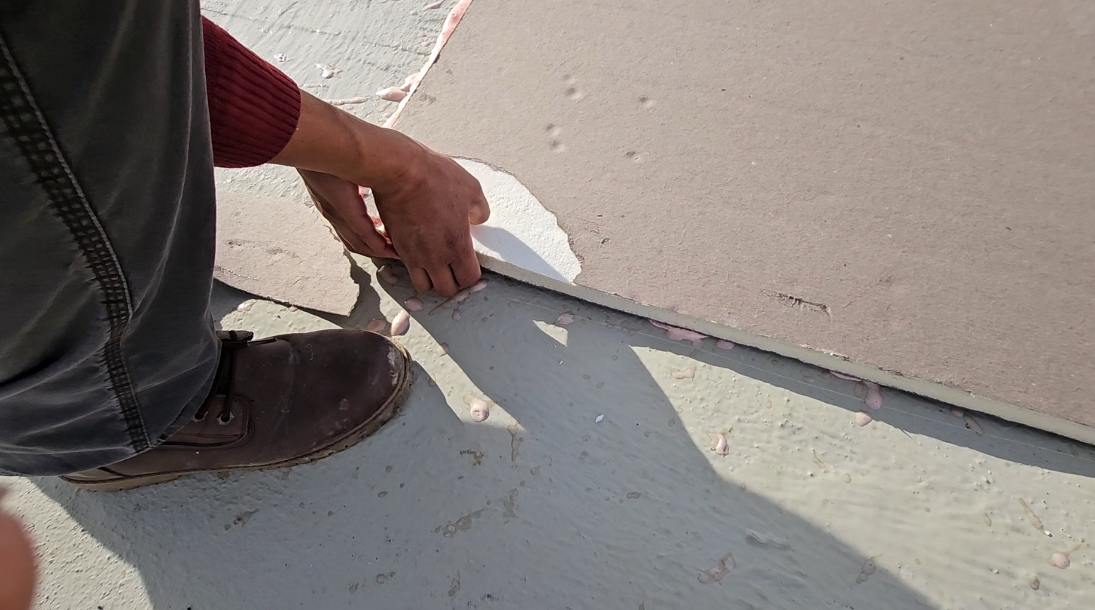 Roofing technician gripping the edge of an adhered polyisocyanurate board to pull-test the bond at 1530 P St NW