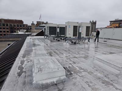 Weathered existing membrane roof at the 1530 P St NW embassy in Washington, DC, with a bank of rooftop HVAC condensing units set on curbs across the field