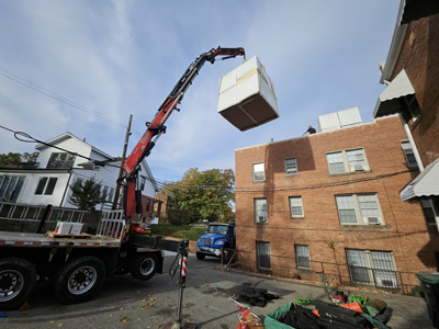 Knuckle-boom crane hoisting a bundle of insulation board to the roof of the apartment building at 2801 Pennsylvania Ave SE