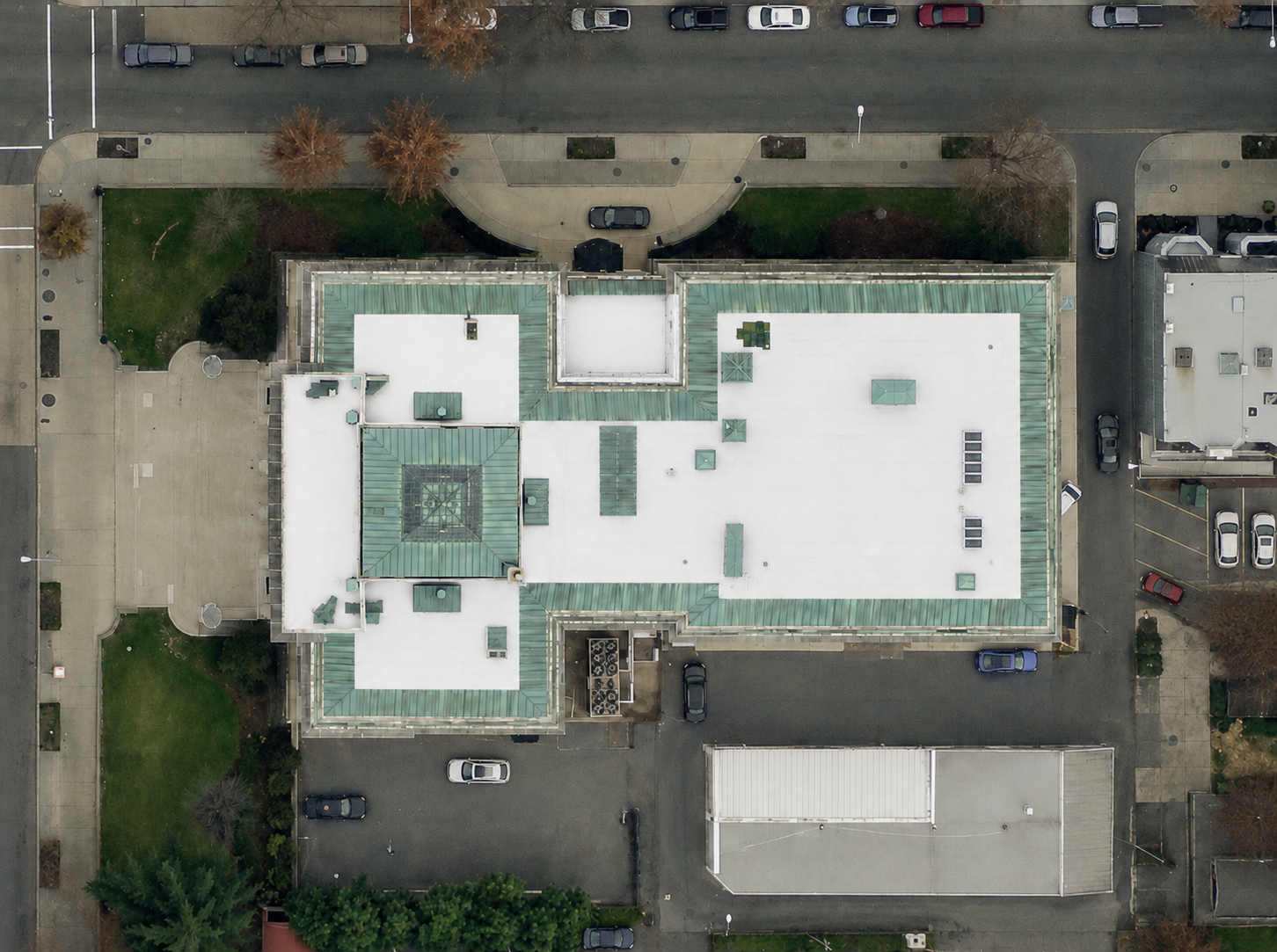 Overhead drone view of the embassy building at 1530 P St NW, Washington DC, with new white TPO roof sections framed by green patinated standing seam roofs